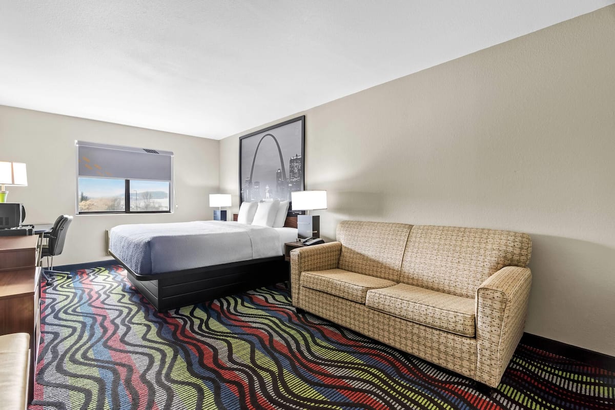 Une chambre d’hôtel avec un lit, un canapé, un bureau et une fenêtre donnant sur le paysage urbain.