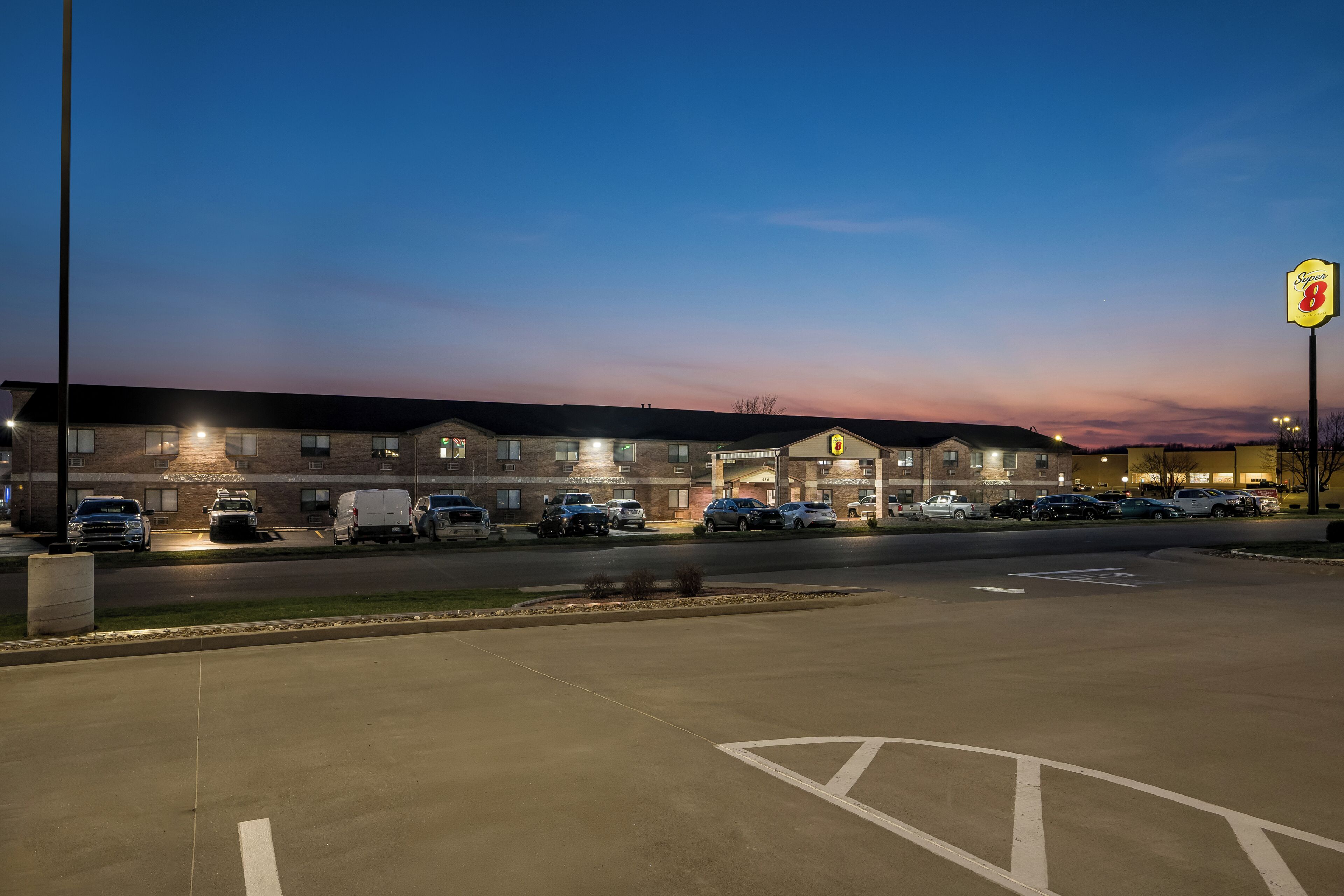 Een hotel met een parkeerplaats, meerdere voertuigen en een bord met de naam van het hotel.
