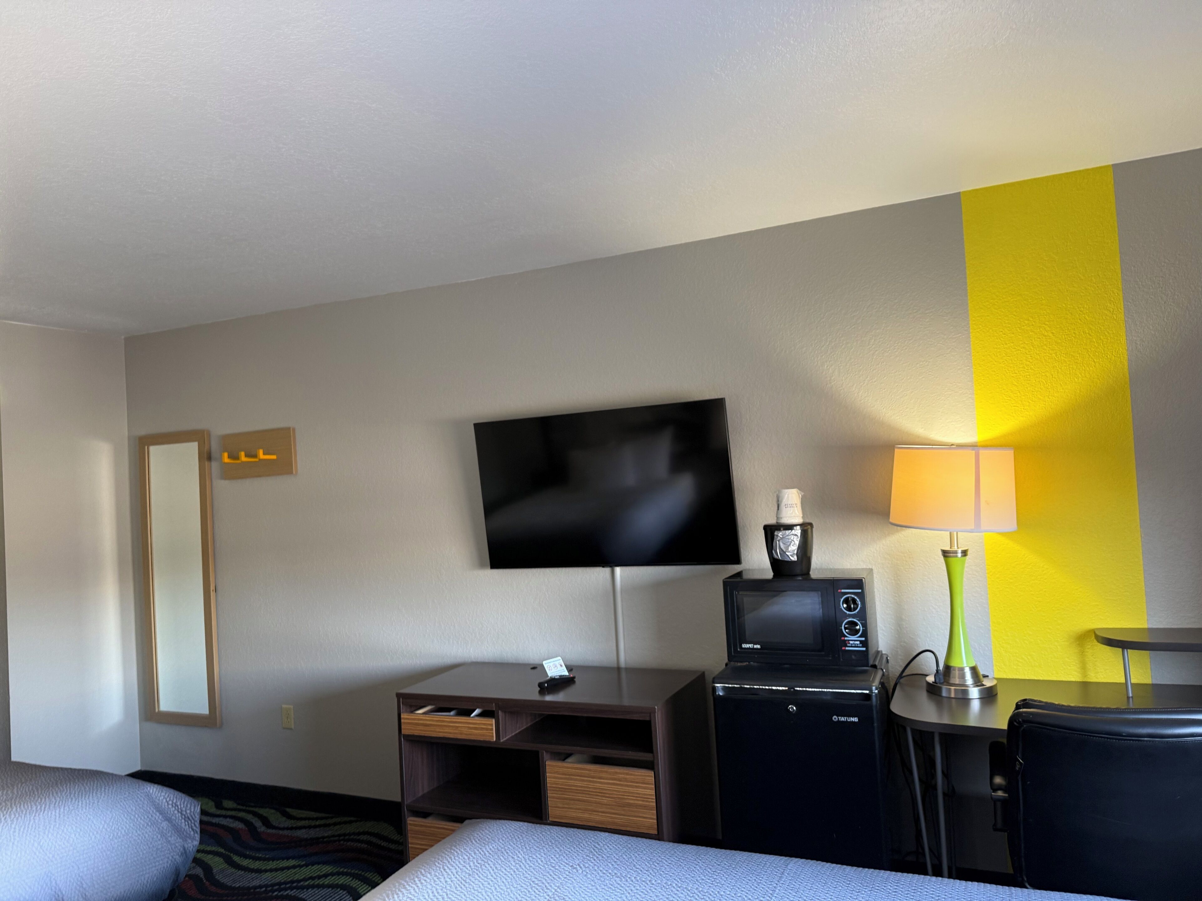 Ein Hotelzimmer mit einem Bett, einem Schreibtisch mit Computer, einem Fernseher, einer Lampe und einer Minibar.