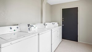A laundry room with a front-loading washer and dryer, a door, and a light fixture. - Super 8 by Wyndham Farmington (Farmington)