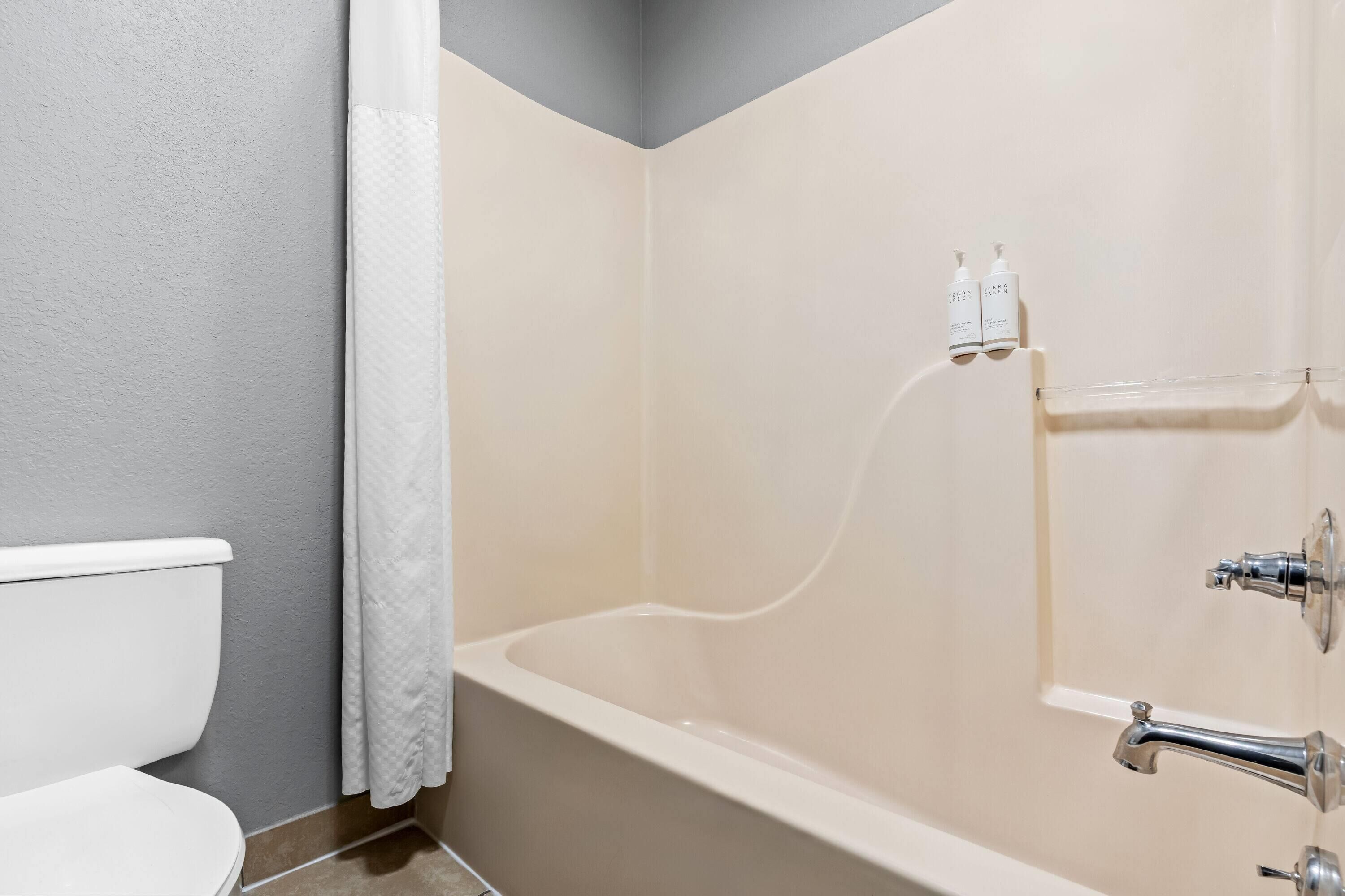 Et badeværelse med badekar, toilet og bruseforhæng.