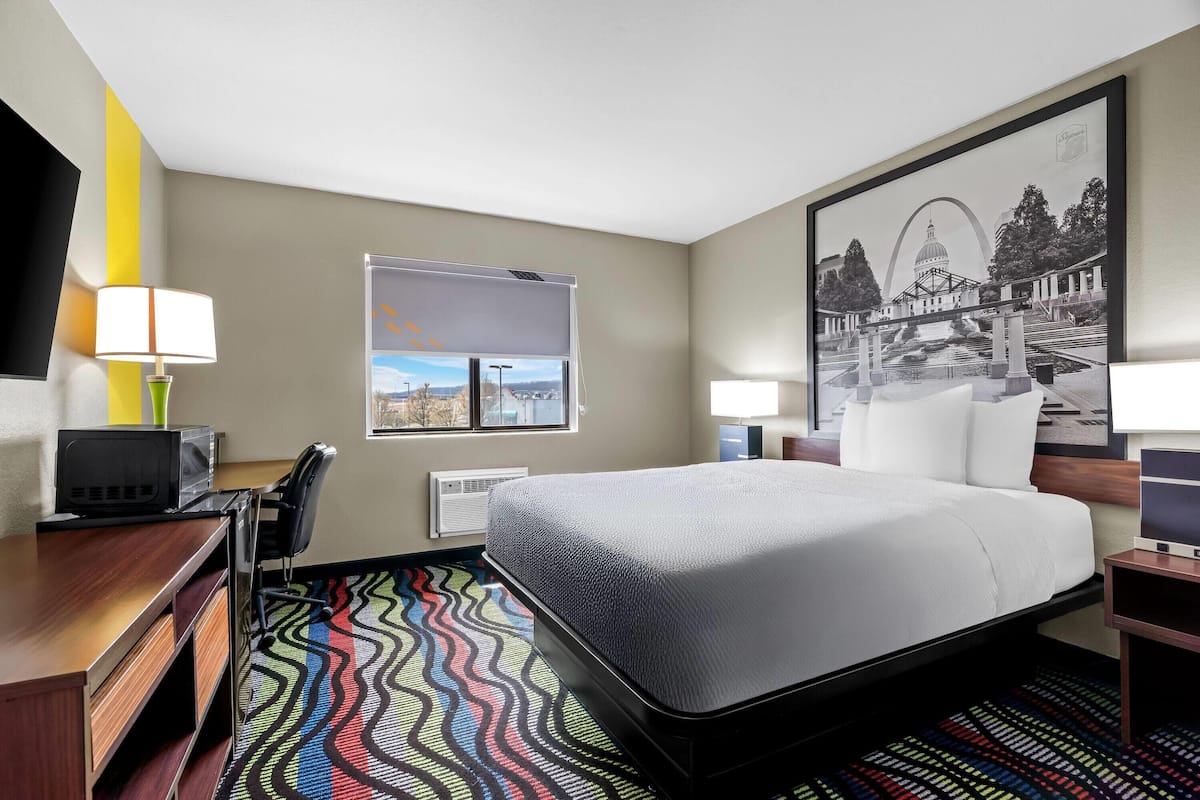 Une chambre d’hôtel équipée d’un lit, d’un bureau, d’une chaise et d’une grande fenêtre donnant sur un beau paysage.