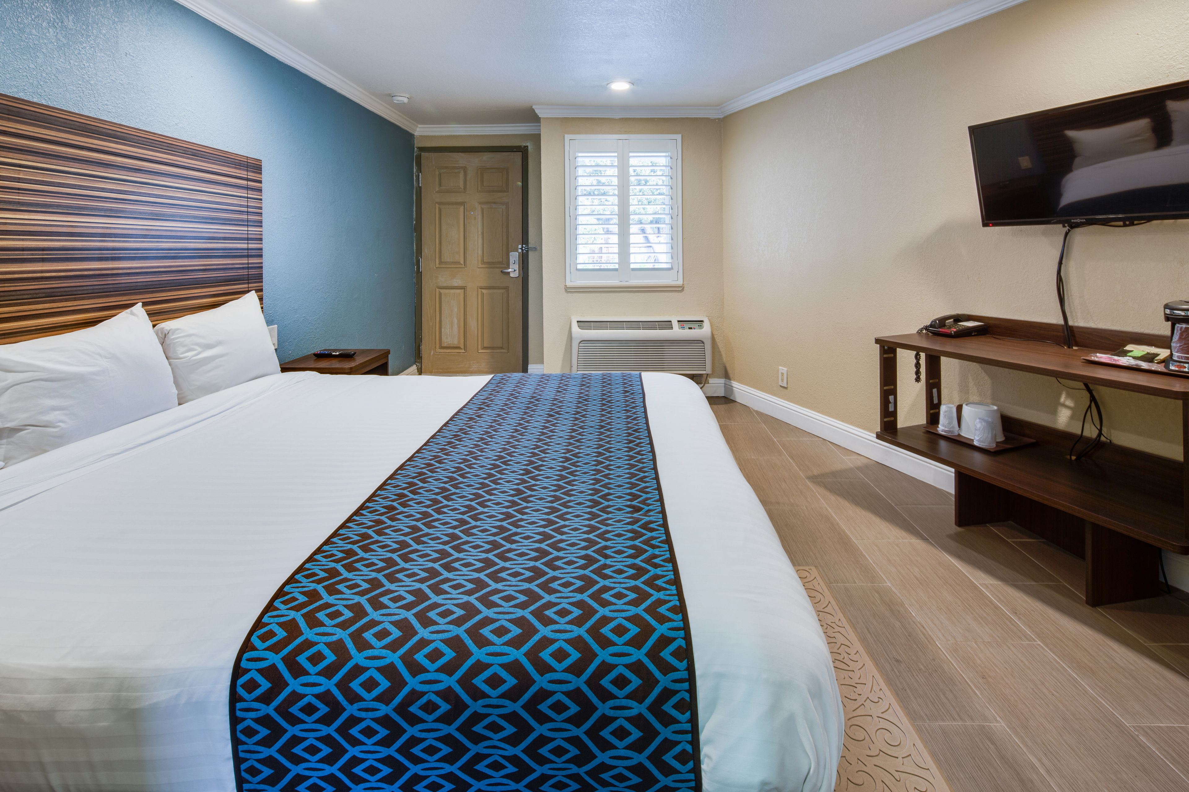 Hotelkamer met een groot bed, een televisie, een bureau met een computer en een raam met zonwering.