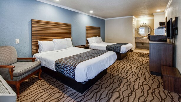 A hotel room with two beds, a chair, a desk, a television, and a bathroom with a mirror and sink. - Americas Best Value Inn Richmond San Francisco (Richmond)
