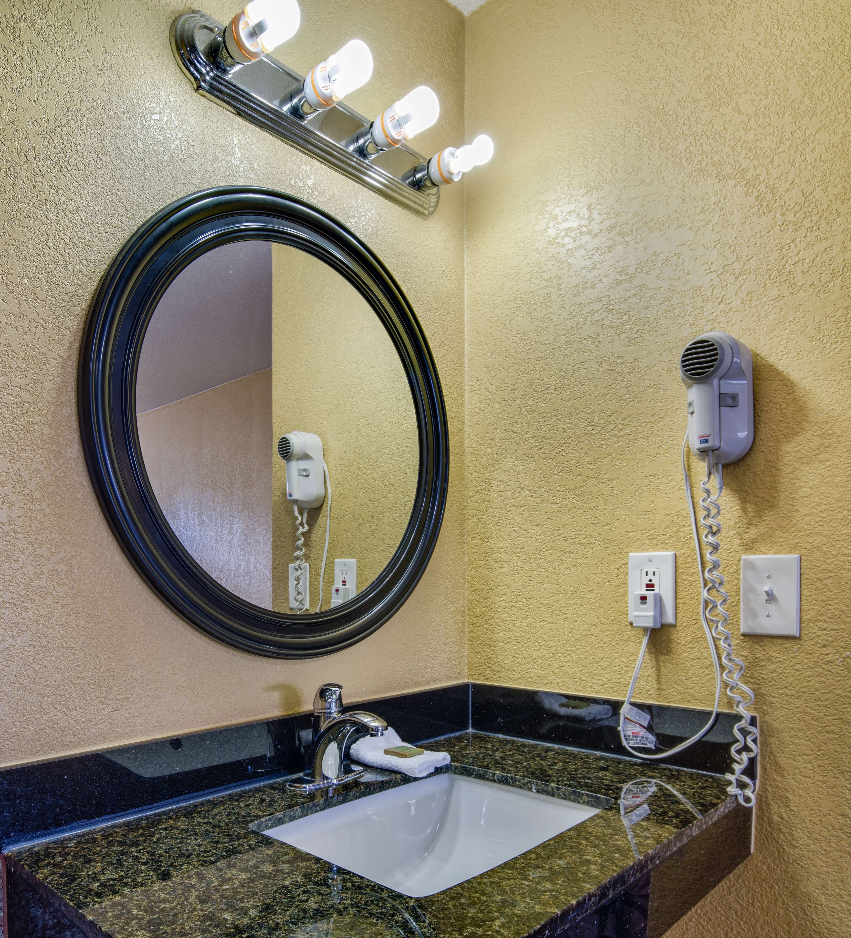 A bathroom with a round mirror, a sink, a hairdryer, and a light fixture above the mirror.