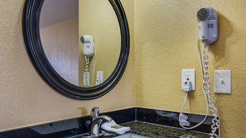 A bathroom with a round mirror, a sink, a hairdryer, and a light fixture above the mirror.