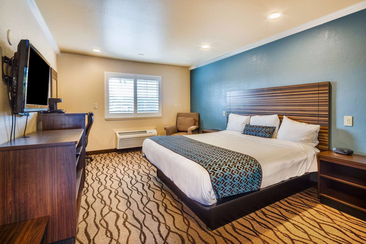 A hotel room with a bed, a desk, a chair, a TV, and a window with blinds.
