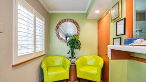 A reception area with two bright yellow chairs, a potted plant, and a mirror on the wall. - Americas Best Value Inn Richmond San Francisco (Richmond)