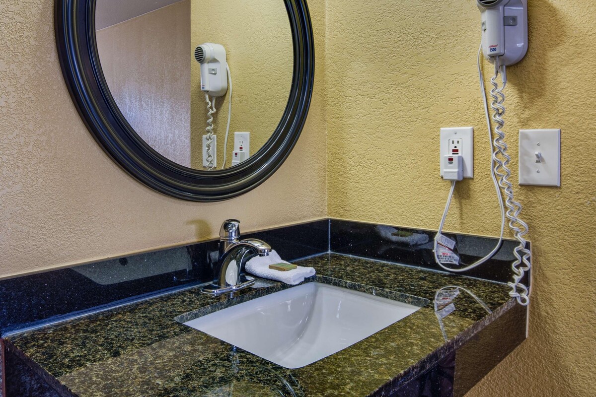 A bathroom with a round mirror, a sink, a hairdryer, and a light fixture.
