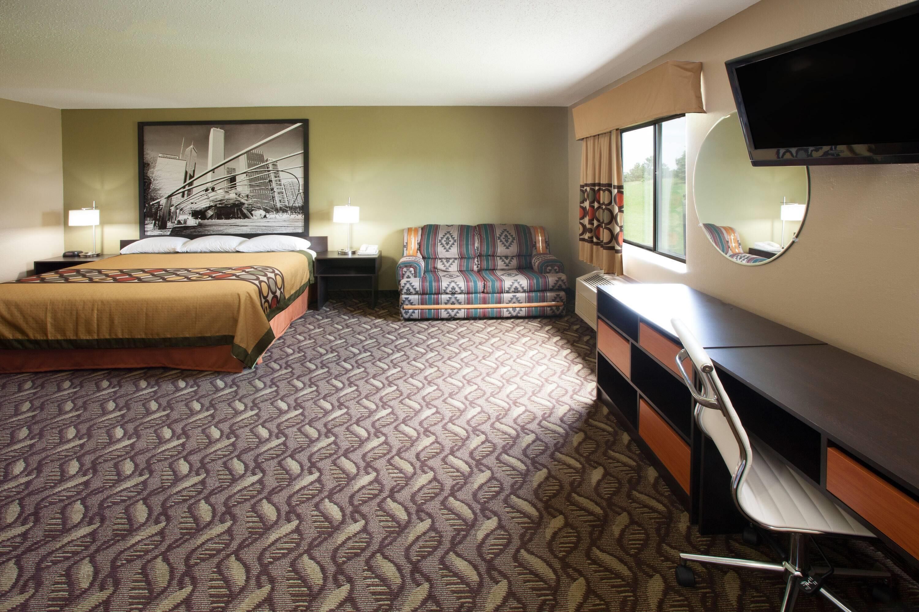 A hotel room with a bed, a sofa, a desk, and a TV.