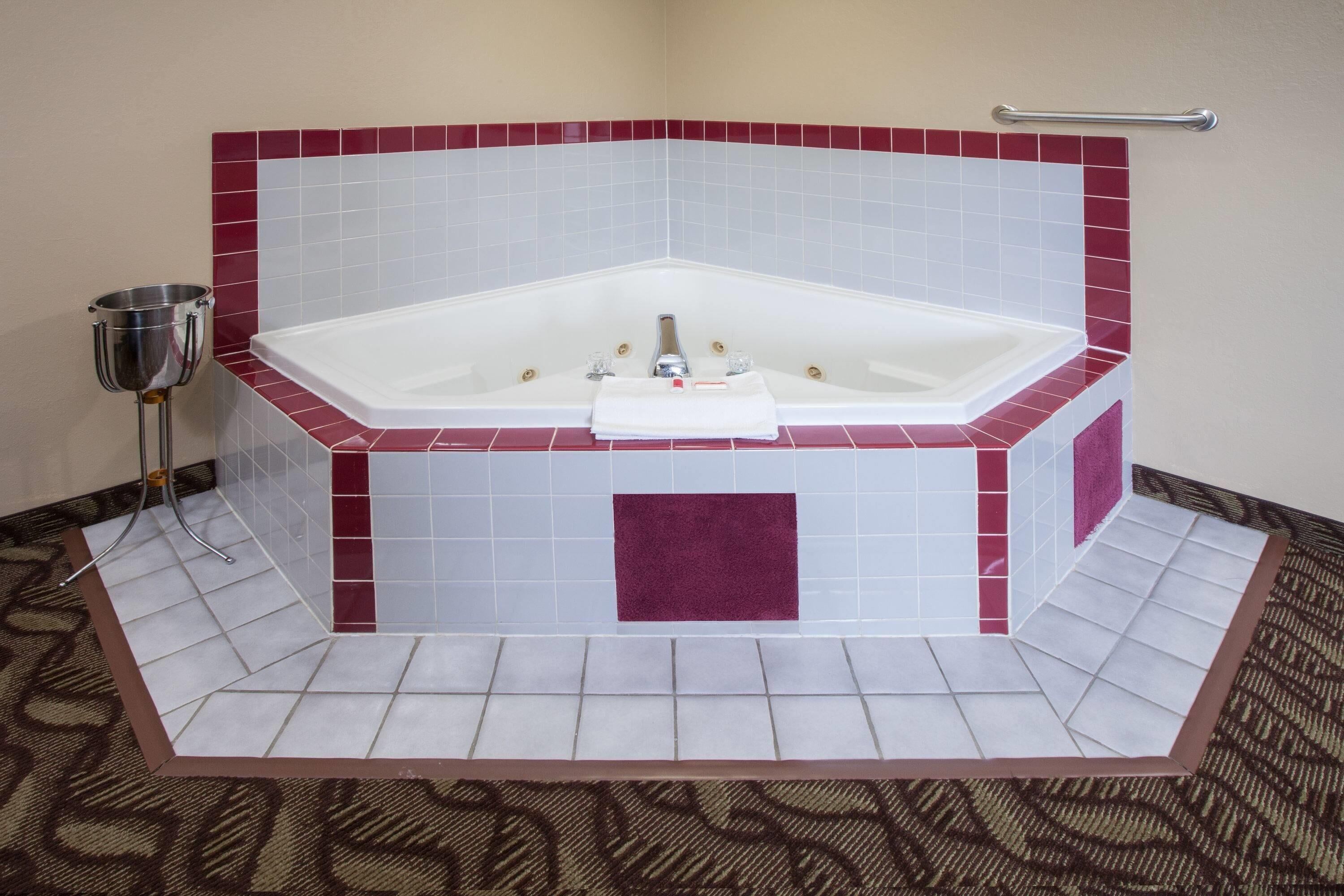 Una bañera con forma de esquina, con diseño de azulejos blancos y rojos, una toalla y un cubo de metal.