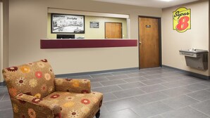 A reception area with a floral-patterned armchair, a reception desk, a wall-mounted sign, and a door.