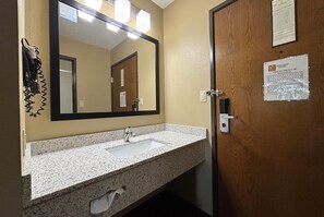 A bathroom with a granite countertop sink, a large mirror, and a wooden door. - Super 8 by Wyndham Dwight (Dwight)