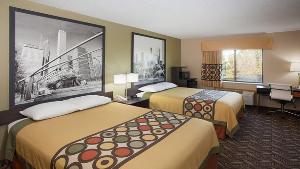 A hotel room with two beds, a cityscape painting, a desk, and a chair.