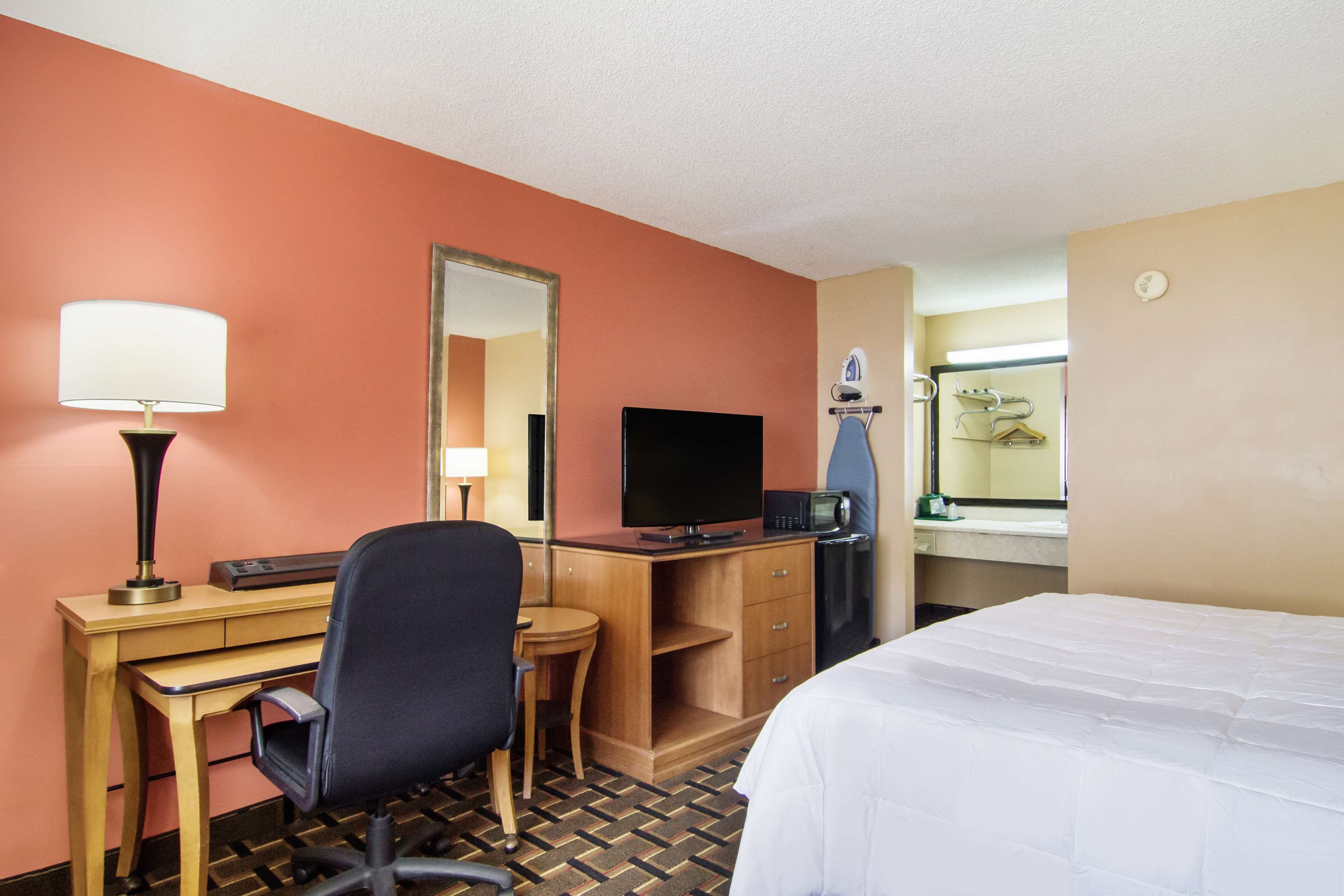 Habitación de hotel con escritorio, silla, televisor, microondas y cama.