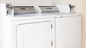 A front view of a white, modern laundry room with a large washing machine and dryer, a control panel, and a small cabinet. - Americas Best Value Inn Darien (Darien)