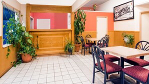 A dining area with a wooden bench, red upholstered chairs, and potted plants.