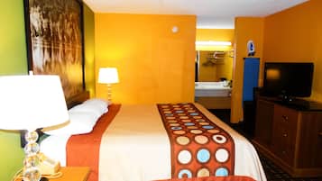 Habitación de hotel con cama, televisor, lámpara, espejo y baño visible a través de una puerta abierta.