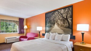 A hotel room with a large bed, two bedside lamps, a window with curtains, a chair, and a large framed picture on the wall. - Americas Best Value Inn Darien (Darien)