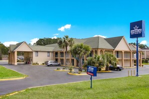 A motel with a central entrance, multiple parking spaces, and a clear sky.
