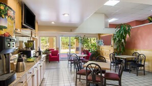 A restaurant with a kitchen area, dining tables, chairs, and a large potted plant. - Americas Best Value Inn Darien (Darien)