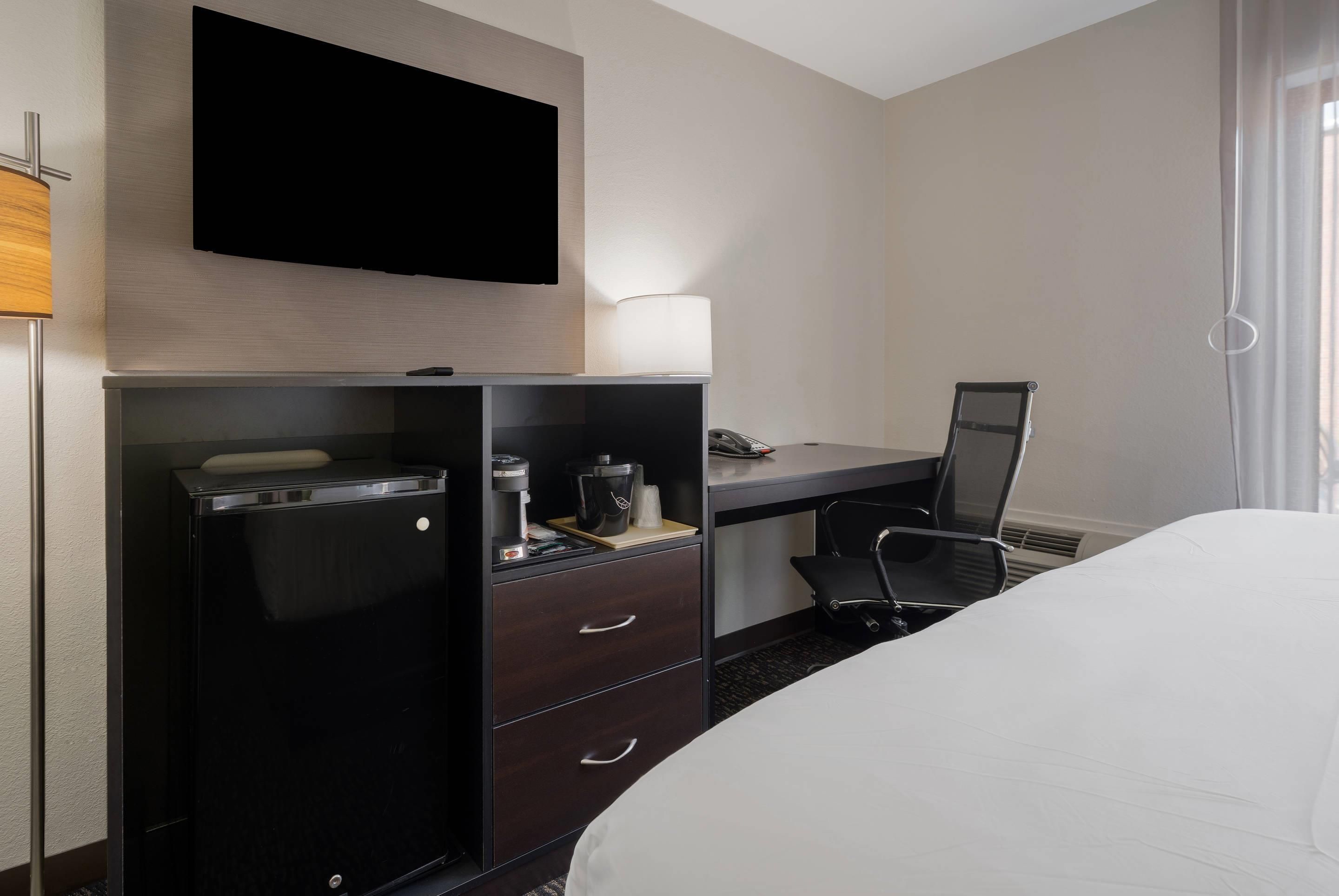 A hotel room with a bed, a desk with a computer, a television, and a coffee machine.