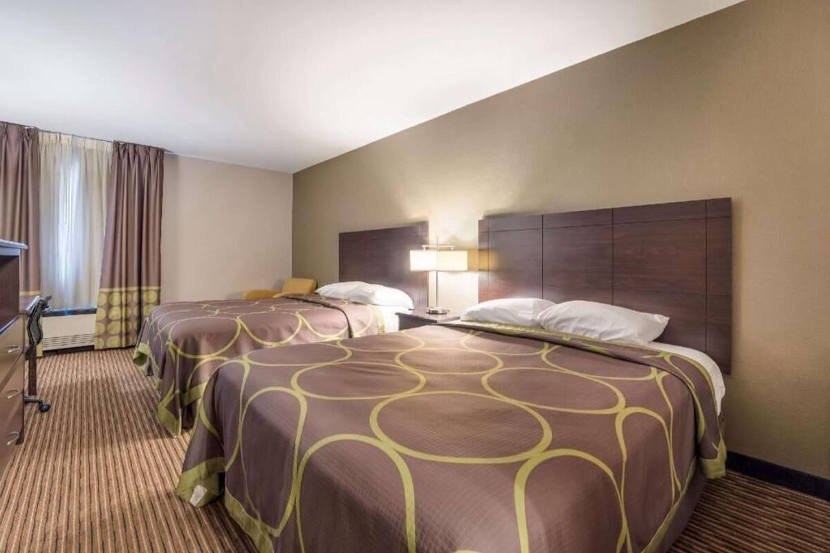 A hotel room with two beds, a desk, a lamp, and a window with curtains.