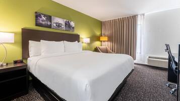 A hotel room with a large bed, two bedside tables, a chair, a desk, a lamp, a painting, and a window with curtains.