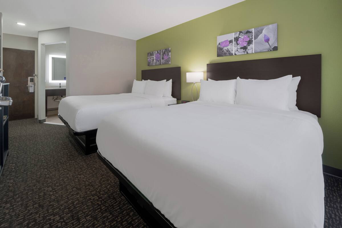 A hotel room with two beds, a bathroom, and a hallway.
