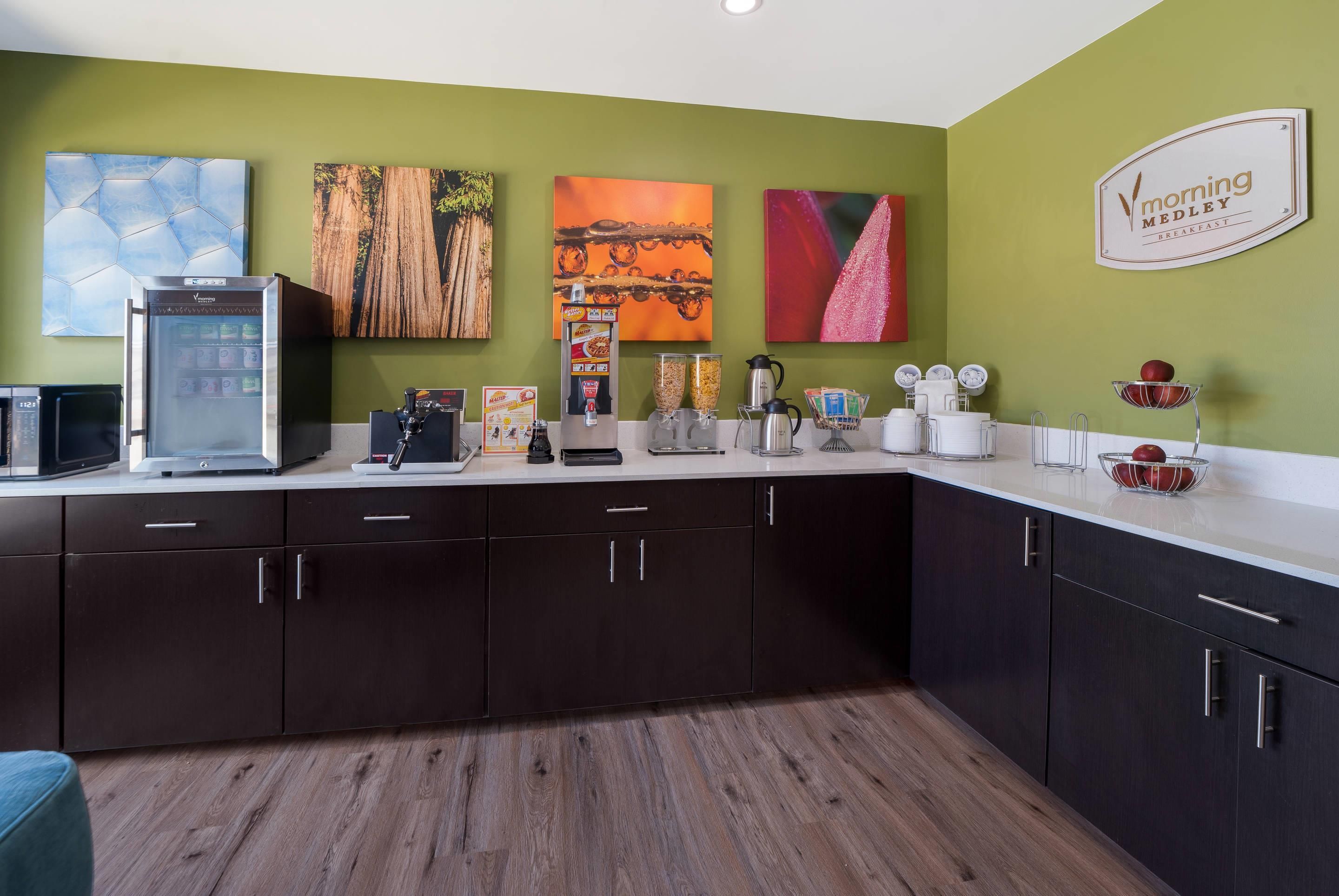 A kitchen with a coffee machine, a microwave, and a refrigerator. There are cabinets and a countertop with various items on it.