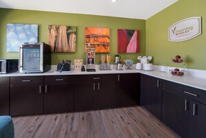A kitchen with a coffee machine, a microwave, and a refrigerator. There are cabinets and a countertop with various items on it.