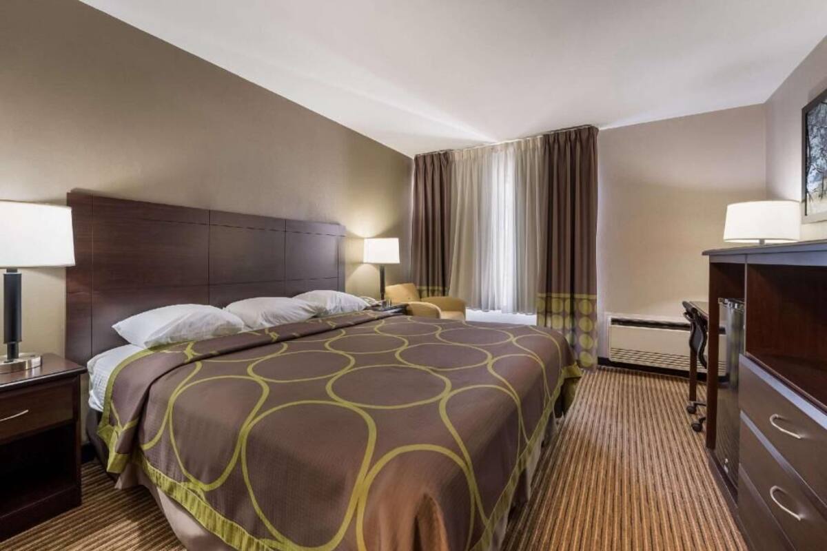 A hotel room with a bed, a desk, a chair, a TV, and a window with curtains.