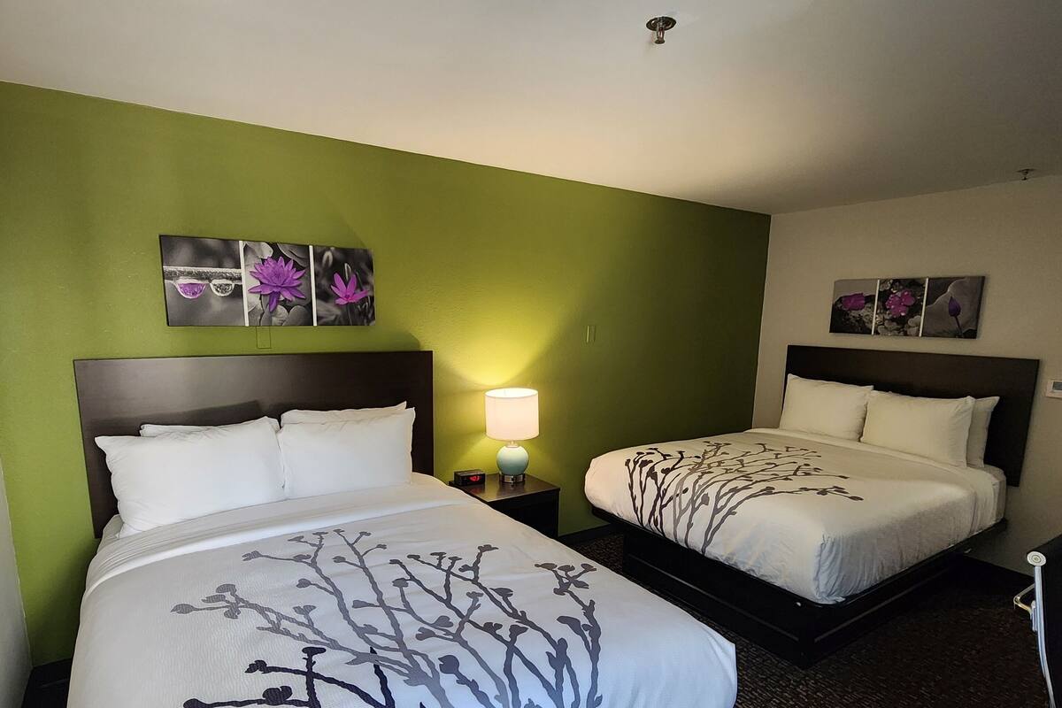 A hotel room with two beds, green walls, and artwork on the walls.