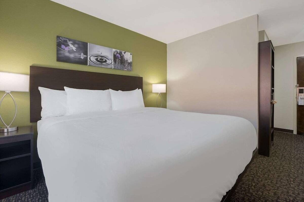 A hotel room with a large bed, two wall-mounted lamps, and three framed pictures above the bed.