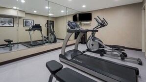 A gym with a treadmill, elliptical, and stationary bike, a bench, and a mirror reflecting the equipment. - Sleep Inn Madison (Madison)