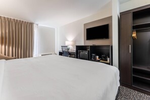 A hotel room with a large bed, a desk with a lamp, a television mounted on the wall, and a wardrobe.