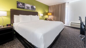 A hotel room with a large bed, two bedside tables with lamps, a chair, a TV, and a window with curtains. - Sleep Inn Madison (Madison)
