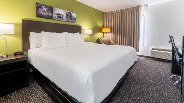 A hotel room with a large bed, two bedside tables with lamps, a chair, a TV, and a window with curtains. - Sleep Inn Madison (Madison)
