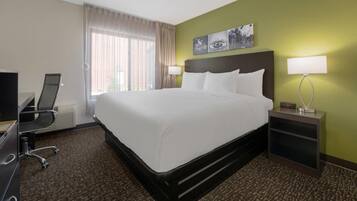 A hotel room with a bed, desk, chair, lamp, and artwork on the wall.