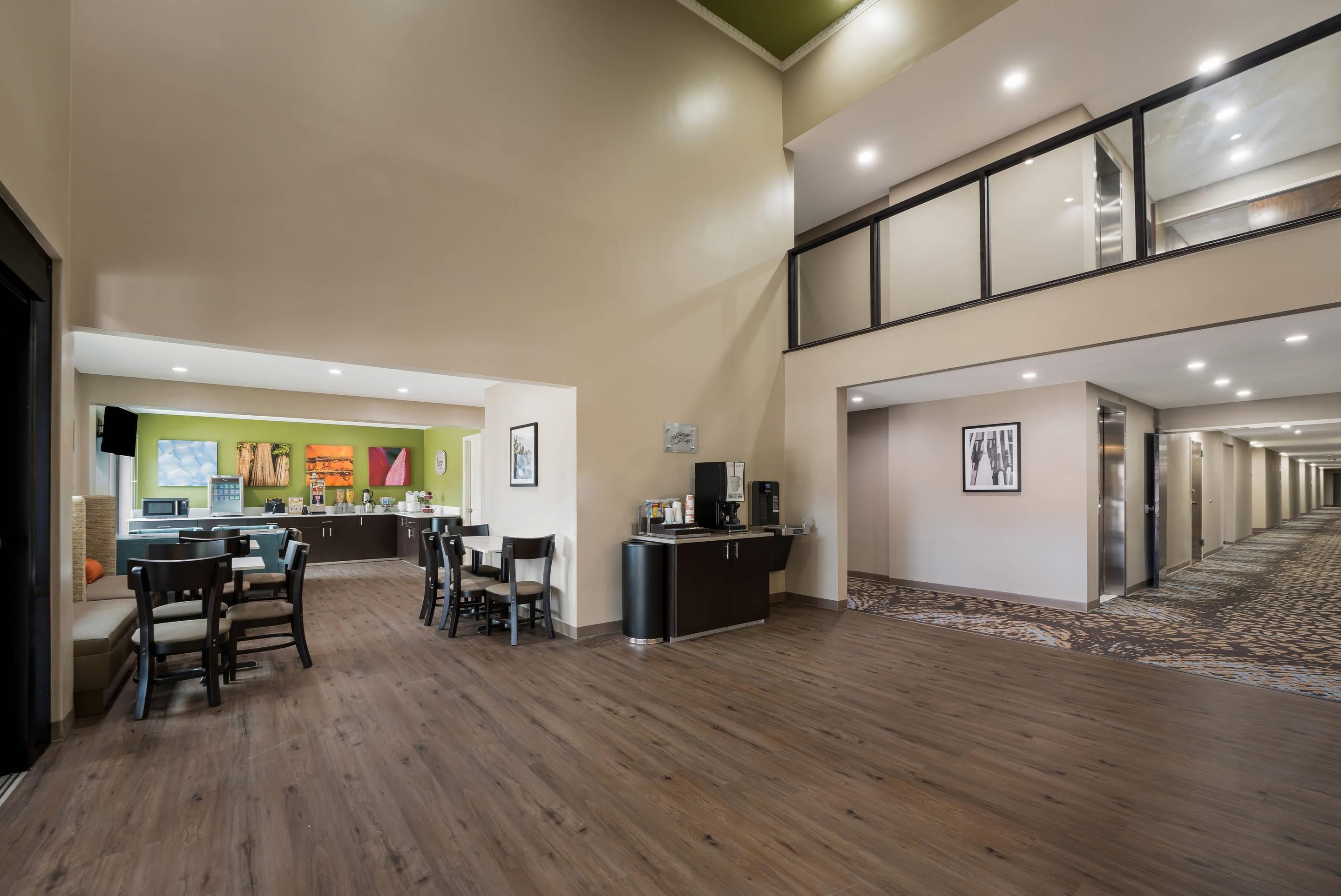 Un vestíbulo de hotel con zona de comedor, una recepción y una escalera que sube a un nivel superior.