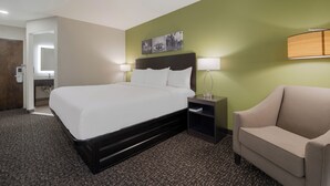 A hotel room with a large bed, a nightstand with a lamp, a chair, and a green accent wall. - Sleep Inn Madison (Madison)