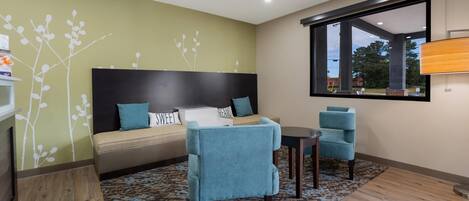 A modern hotel room with a bed, two chairs, a small table, and a large window.