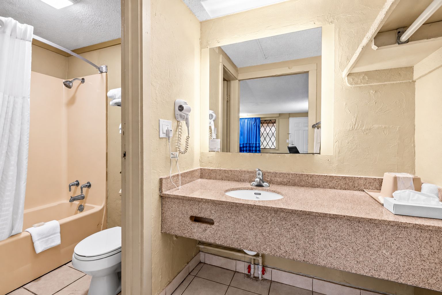 Un baño con ducha, inodoro, lavamanos y un espejo con vista al cuarto.