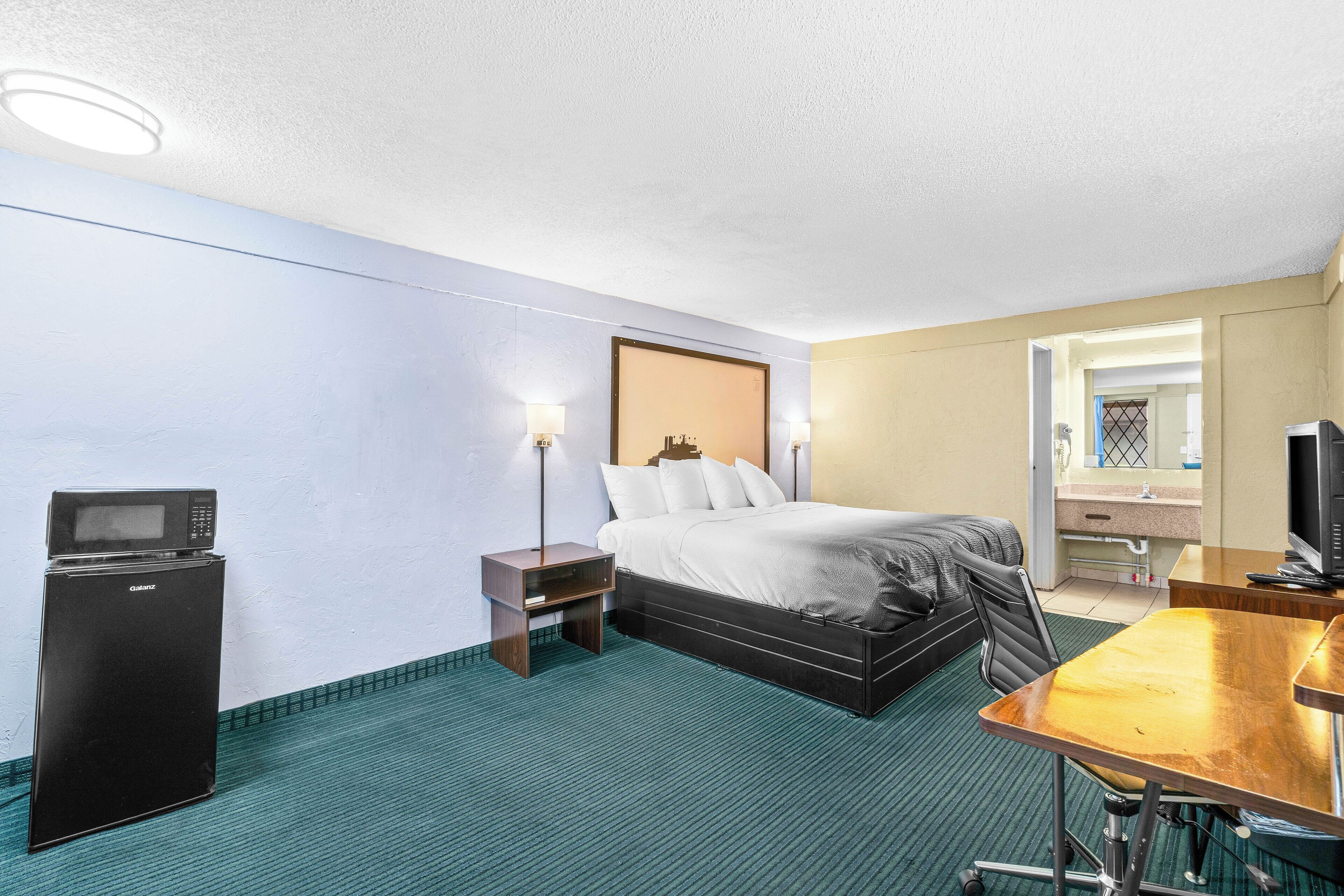 Una habitación de hotel con cama, escritorio, televisor y minibar.