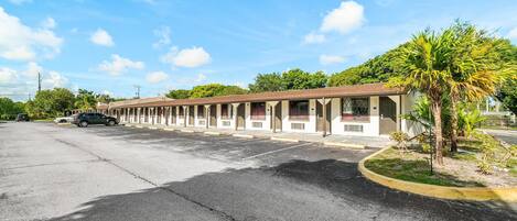 A motel with a row of rooms, a parking lot, and a small garden area.