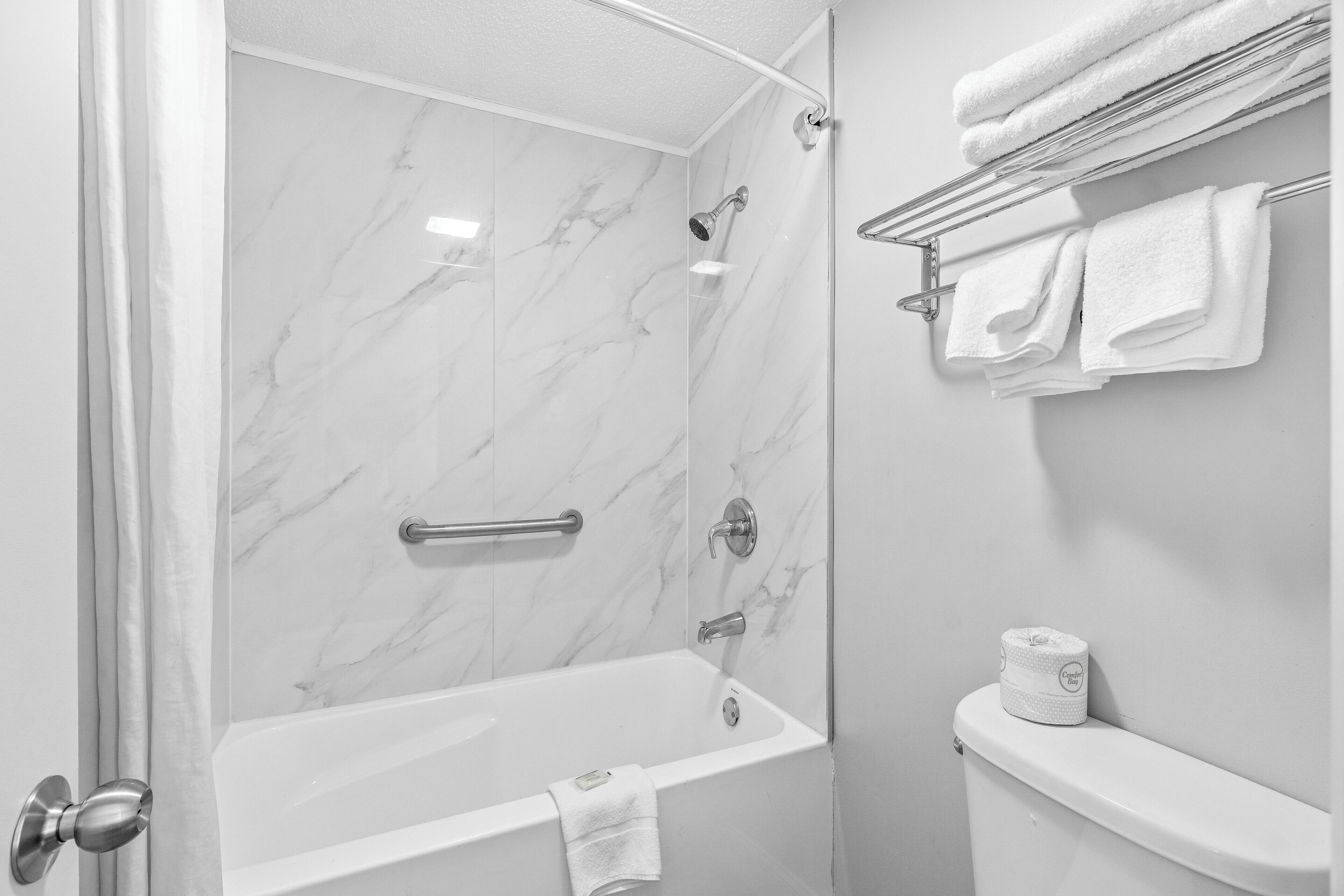 Un baño con pared de ducha de mármol, una bañera, un inodoro y un perchero con toallas.