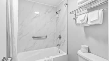 Un baño con pared de ducha de mármol, una bañera, un inodoro y un perchero con toallas.