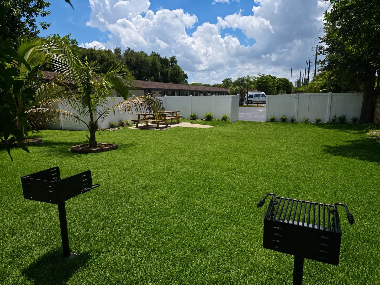 A well-maintained grassy yard with a picnic table, a small palm tree, and a white fence.
