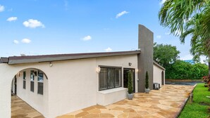 A modern house with a stone patio, a covered entryway, and a large window. - Super 8 by Wyndham Lantana West Palm Beach (Lantana)