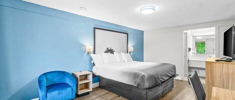 Een moderne hotelkamer met een groot bed, een blauwe fauteuil, een houten bureau en een spiegel.